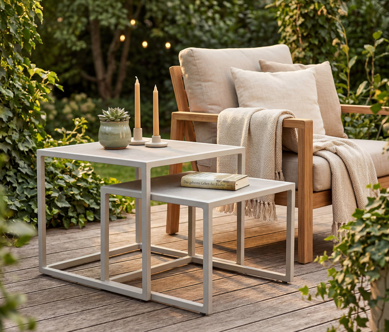 Draußen stehen deVries Beistelltische (2er-Set) neben einem Stuhl mit Kissen und Decke. Auf den Tischen stehen Kerzen, eine Pflanze und ein Buch.