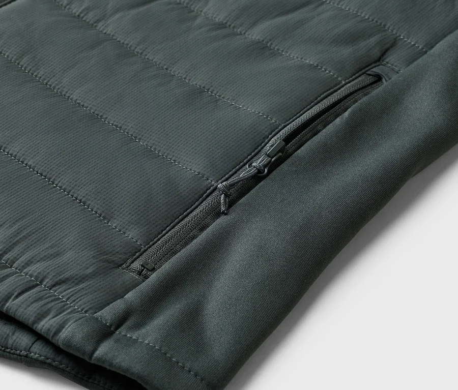 Nahaufnahme einer olivgrünen, gesteppten Jacke mit Reißverschlusstasche am Ärmel.