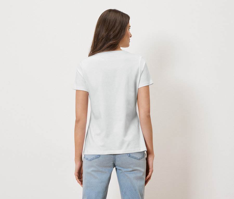 Eine Frau mit langen braunen Haaren trägt ein weißes T-Shirt und blaue Jeans.