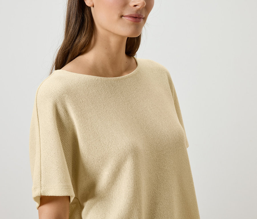 Nahaufnahme einer Frau mit langem, braunem Haar, die ein beigefarbenes Strickoberteil trägt.