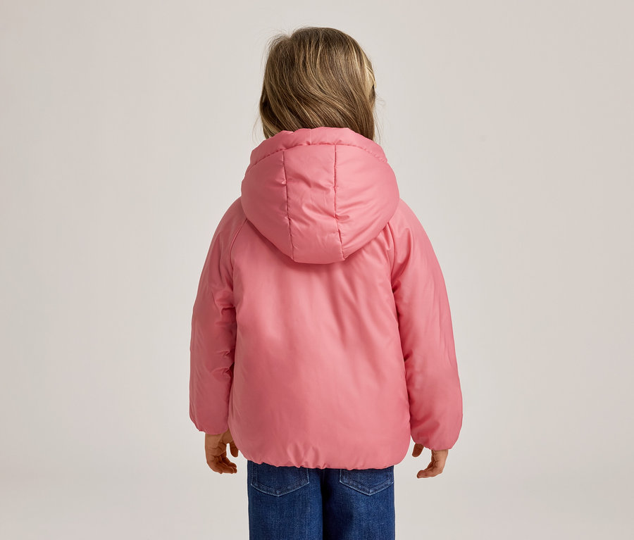 Ein Kind von hinten gesehen, das eine pinkfarbene Kapuzen-Steppjacke und blaue Jeans trägt.
