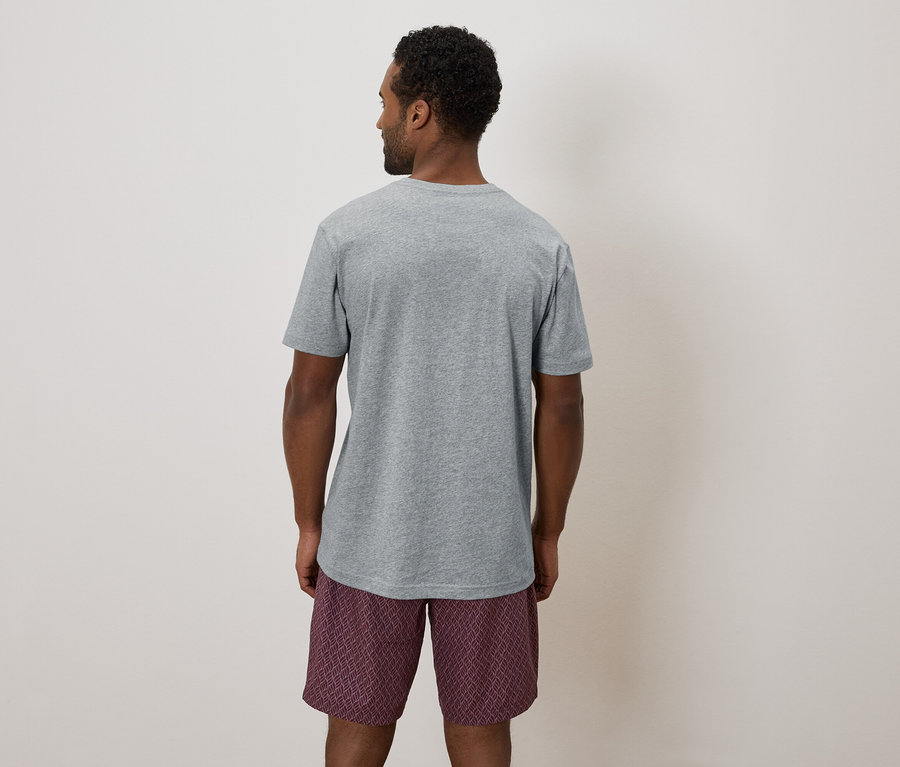 Rückansicht eines Mannes mit grauem T-Shirt und gemusterten Shorts vor einem neutralen Hintergrund.