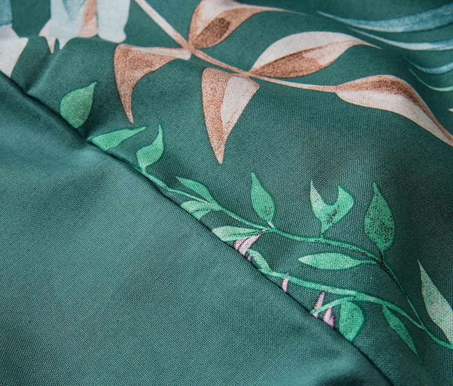 Nahaufnahme eines dunkelgrünen Stoffes, diagonal geteilt. Die obere rechte Hälfte hat ein Blumenmuster mit braunen und grünen Blättern, die untere linke Hälfte ist einfarbig.