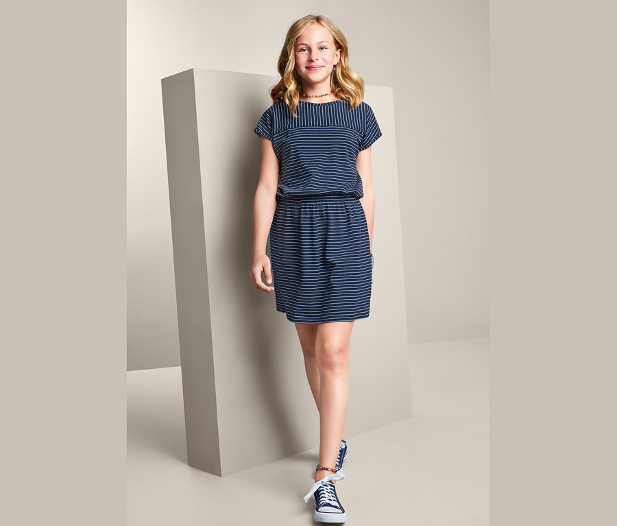 Mädchen posiert stehend in einem gestreiften Jerseykleid.