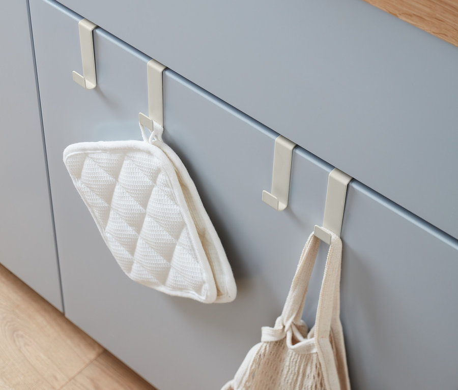 An grauen Küchenschranktüren hängen 4 Türhaken, an denen ein Topflappen und eine Netztasche hängen.