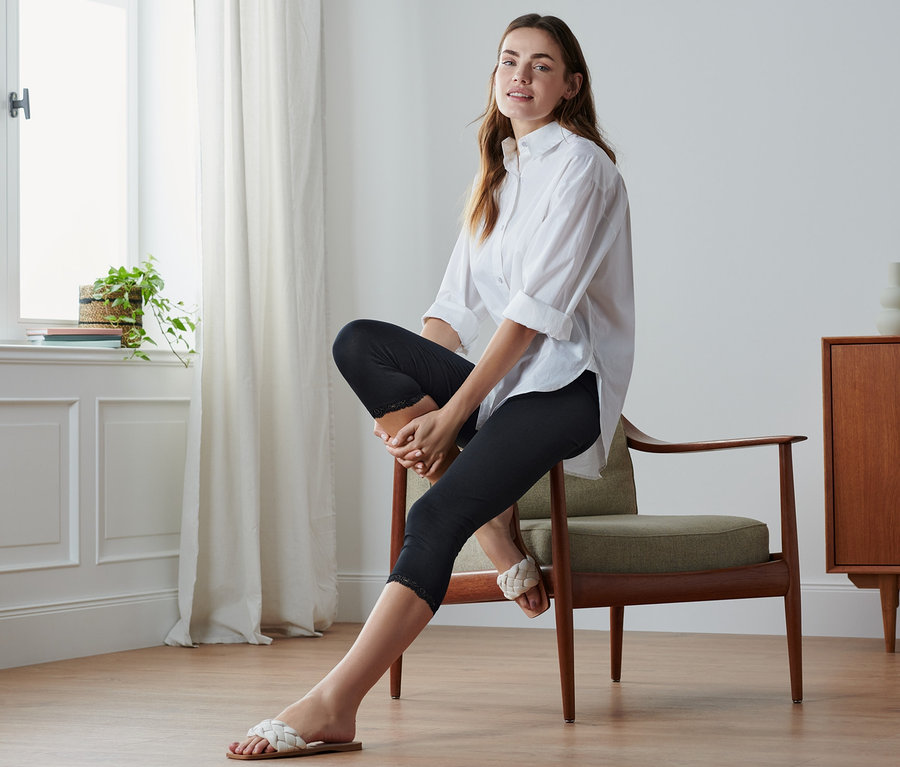Frau sitzt auf Stuhl, trägt schwarze 3/4-Leggings mit Spitzenborte.