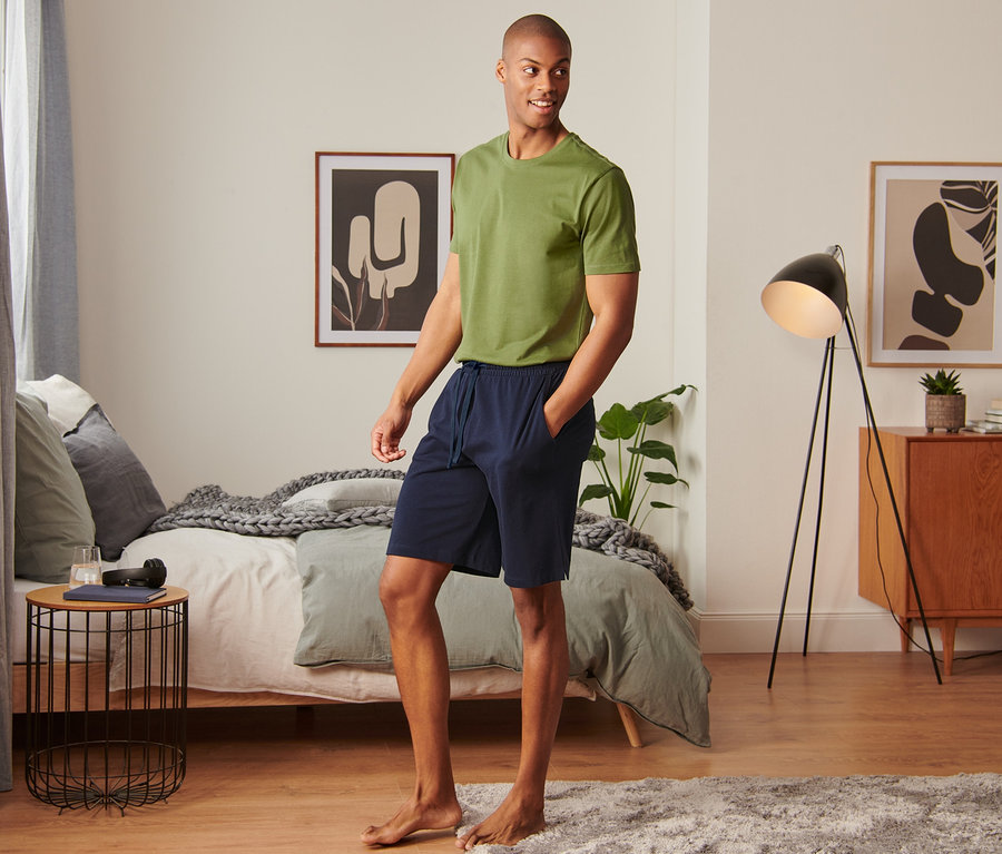 Mann in grünem T-Shirt und dunkelblauen Piqué-Relaxshorts steht im Schlafzimmer.