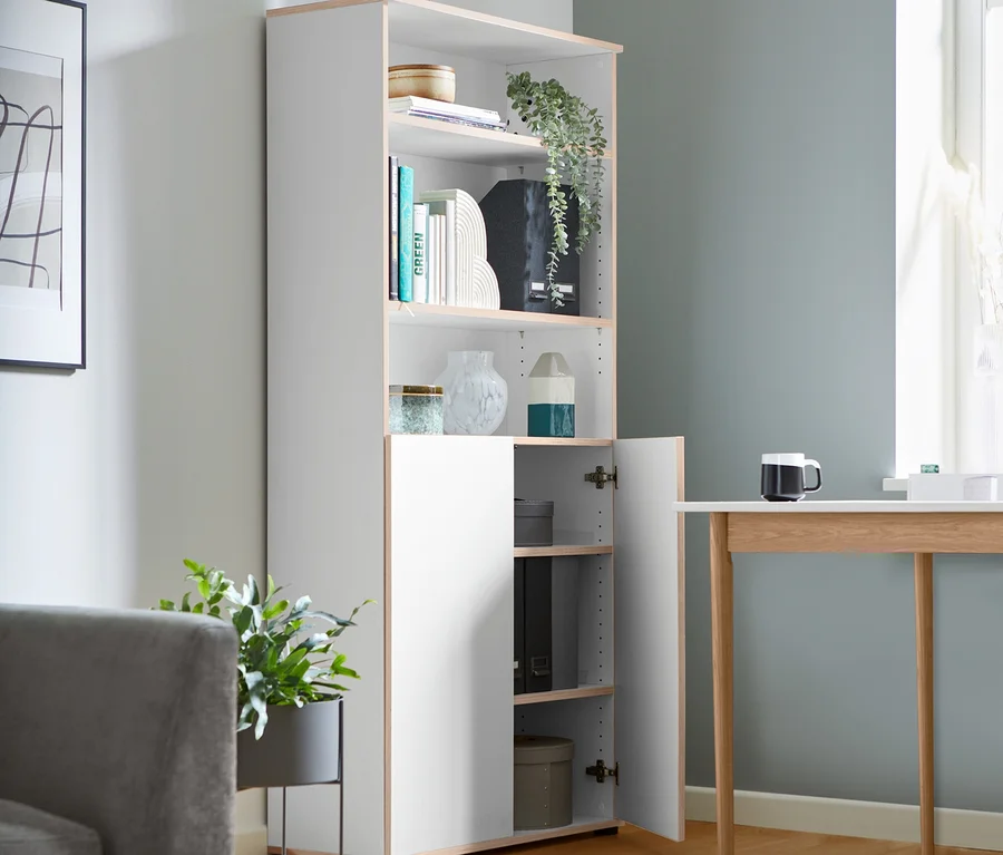Ein hohes, halboffenes Regal mit Büchern und Dekorationen steht in einem Wohnzimmer.
