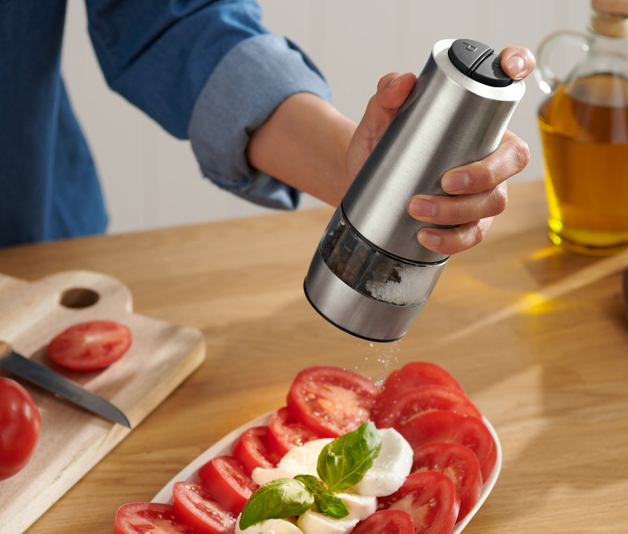 Frau würzt Tomaten und Mozzarella mit einer elektrischen Salz- und Pfeffermühle.