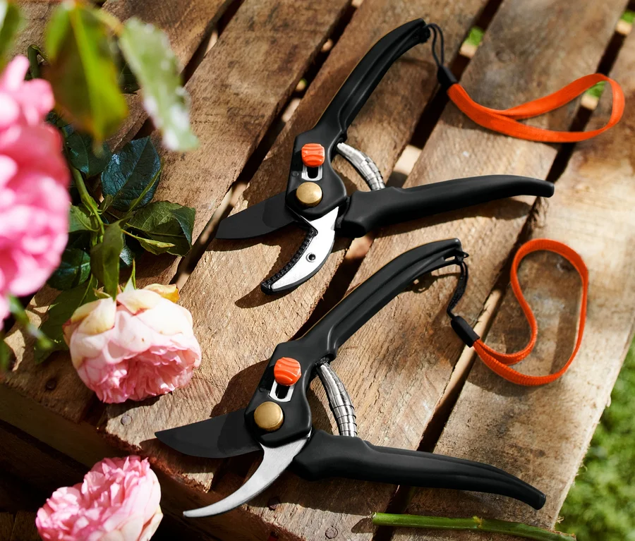 Zwei Gartenscheren auf einer Holzpalette, links rosa Rosen.
