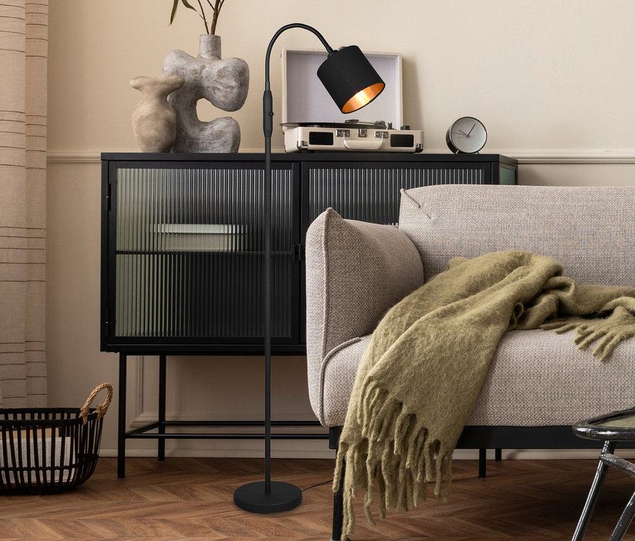 Ein Wohnzimmer mit einem schwarzen Schrank, auf dem ein Plattenspieler, Vasen und eine Uhr stehen. Neben dem Schrank steht eine schwarze Reality Stehleuchte »Tommy«.