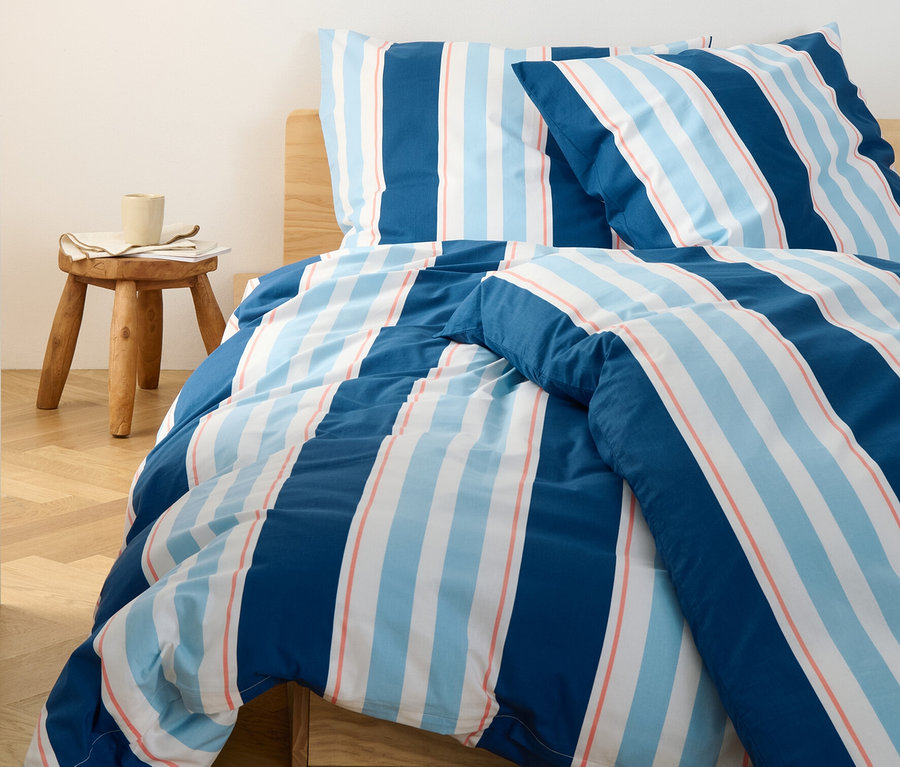 Blau gestreifte Renforcé-Bettwäsche in Normalgröße auf einem Bett. Nachttisch mit Büchern und Lampe.