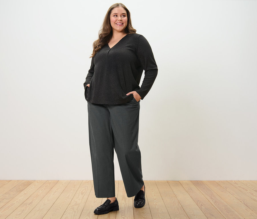 Frau posiert in Komfort-Webhose und glitzerndem Blusenshirt.