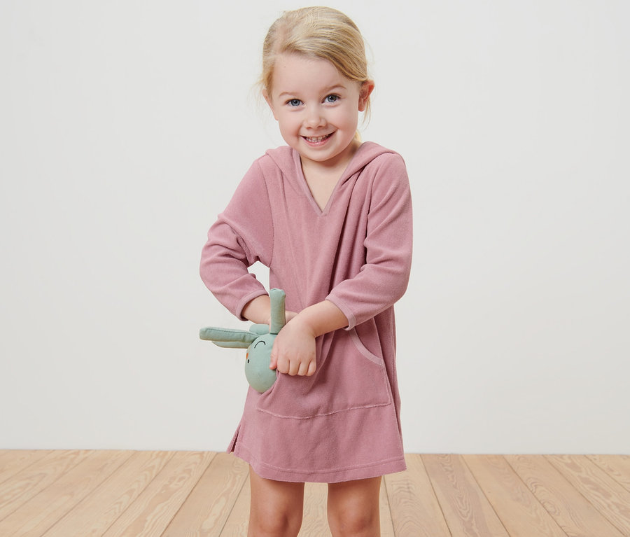 Lächelndes Mädchen trägt einen Kinder-Frottierponcho und hält ein Stoffkaninchen.