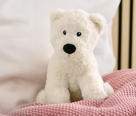 Ein Plüschtier »Eisbär« sitzt auf einer rosafarbenen Strickdecke auf einem Bett.