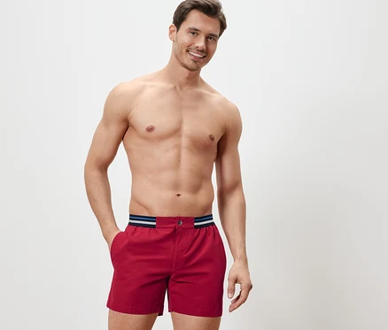 Mann posiert in roten Badeshorts.