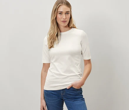Frau posiert in einem cremefarbenen Halbarmshirt und blauen Jeans.