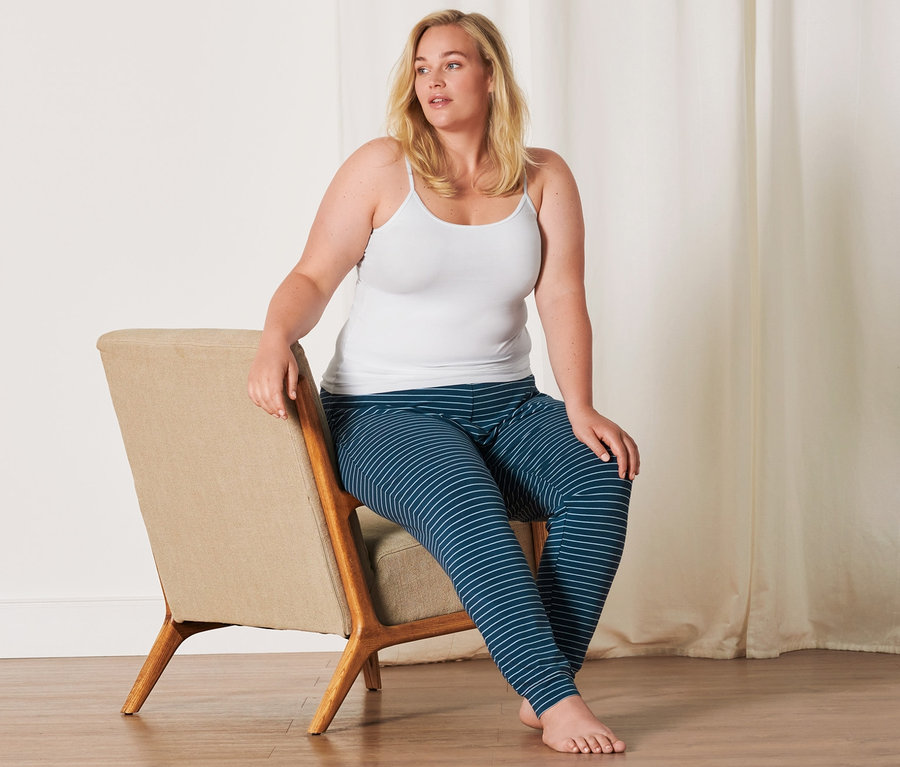 Frau sitzt auf einem Stuhl und trägt ein weißes Hemdchen (2 Hemdchen, weiß) und eine gestreifte Hose.
