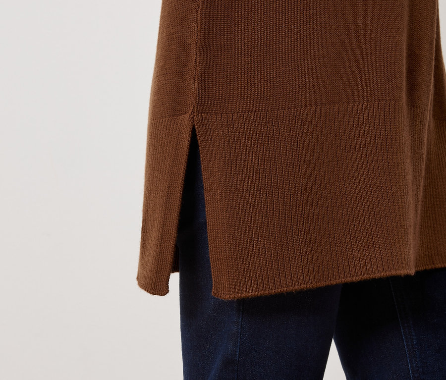 Detail eines braunen Pullovers mit Schlitz an der Seite und dunkelblauen Jeans.