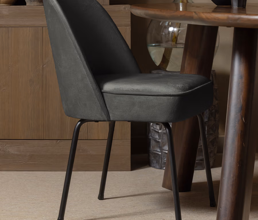 Ein dunkelgrüner BePureHome Esszimmerstuhl »Vogue« steht neben einem Holztisch.