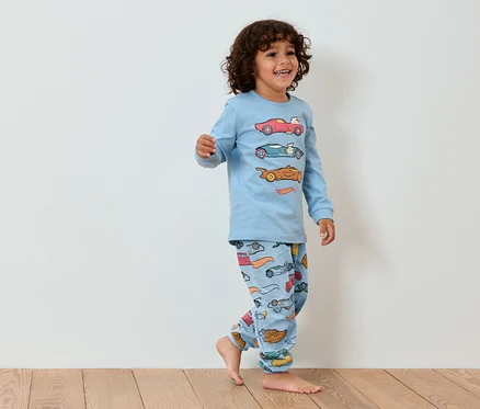 Lächelnder kleiner Junge in blauem Auto-Pyjama geht auf Holzboden.