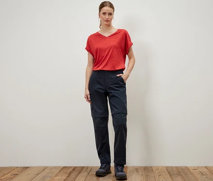 Frau steht in rotem T-Shirt und blauer 2-in-1-Funktionshose.