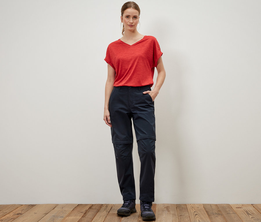 Frau steht in rotem T-Shirt und blauer 2-in-1-Funktionshose.