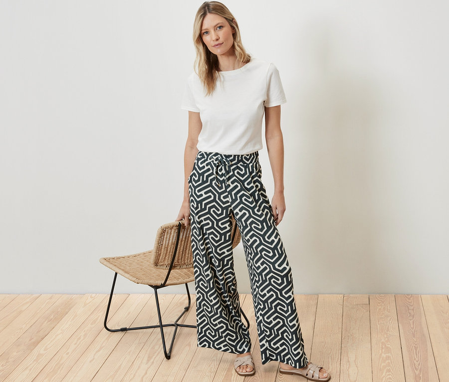 Eine Frau steht und trägt ein weißes T-Shirt und eine bedruckte Schlupfhose in Crinkle-Optik.