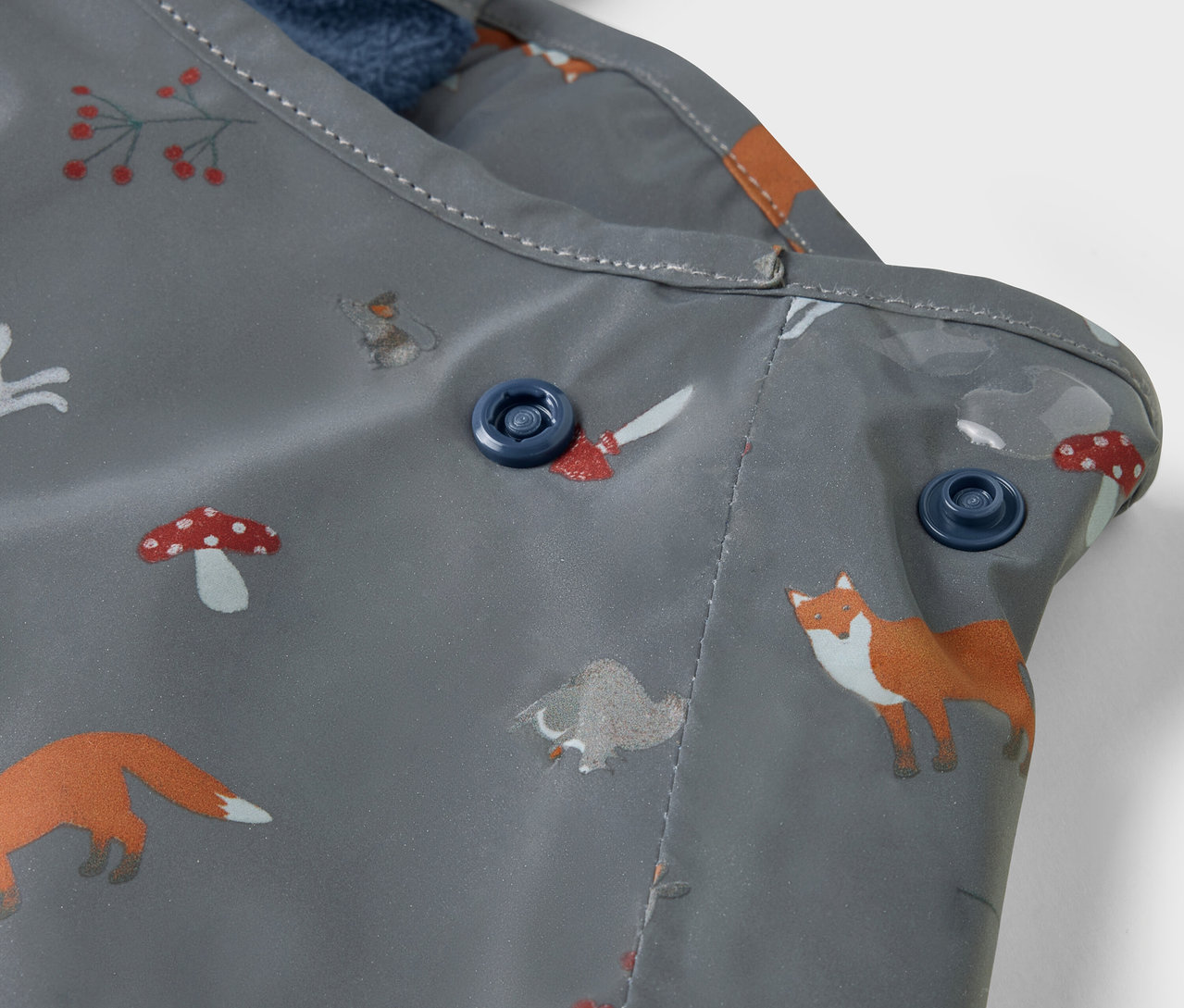 Detailaufnahme einer Kinder-Thermo-Regenhose mit reflektierenden Designelementen und Fuch- und Pilzprint.