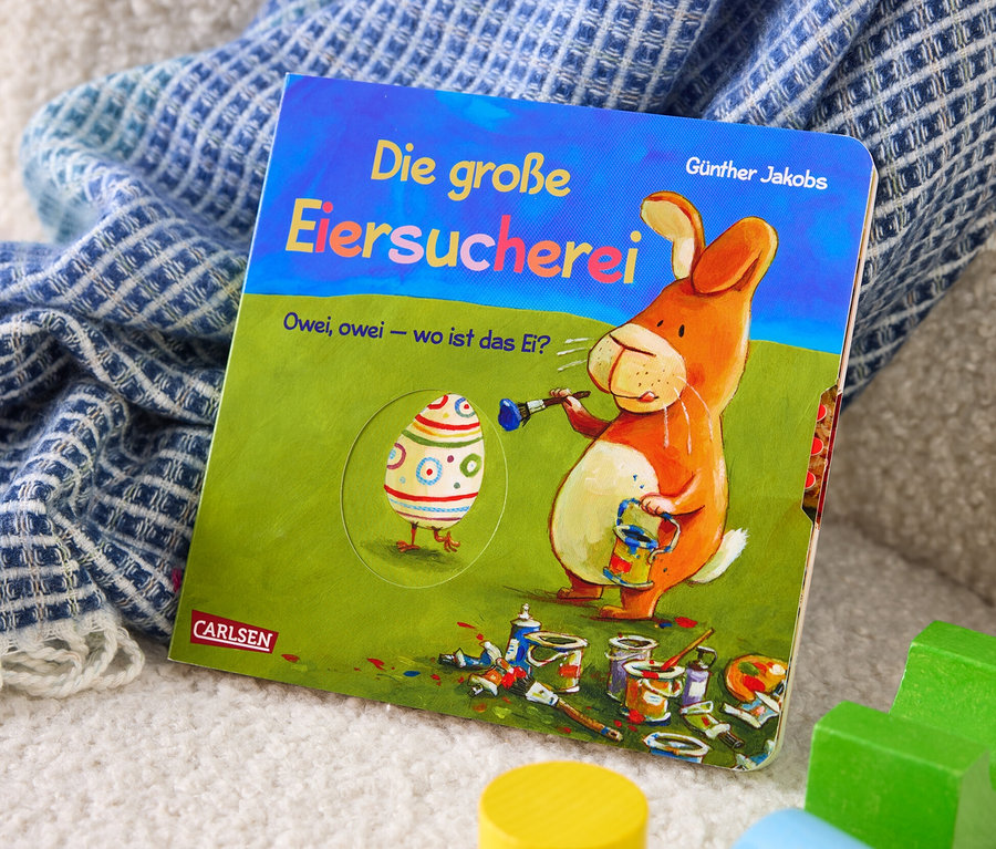 Das Buch »Die große Eiersucherei« liegt auf einer Decke neben Holzbausteinen.