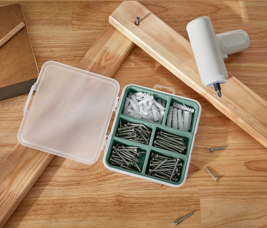 Ein geöffnetes Schrauben- und Dübelset liegt neben Holzbrettern und einem Akku-Schraubendreher.