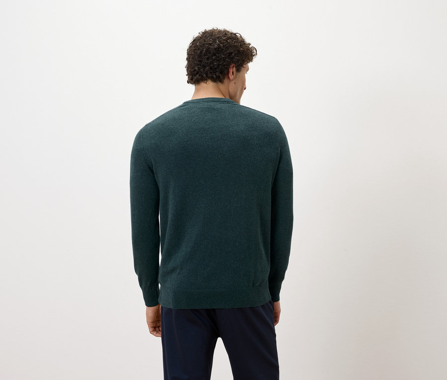Ein Mann mit dem Rücken zur Kamera trägt einen dunkelgrünen Pullover und dunkelblaue Hosen.