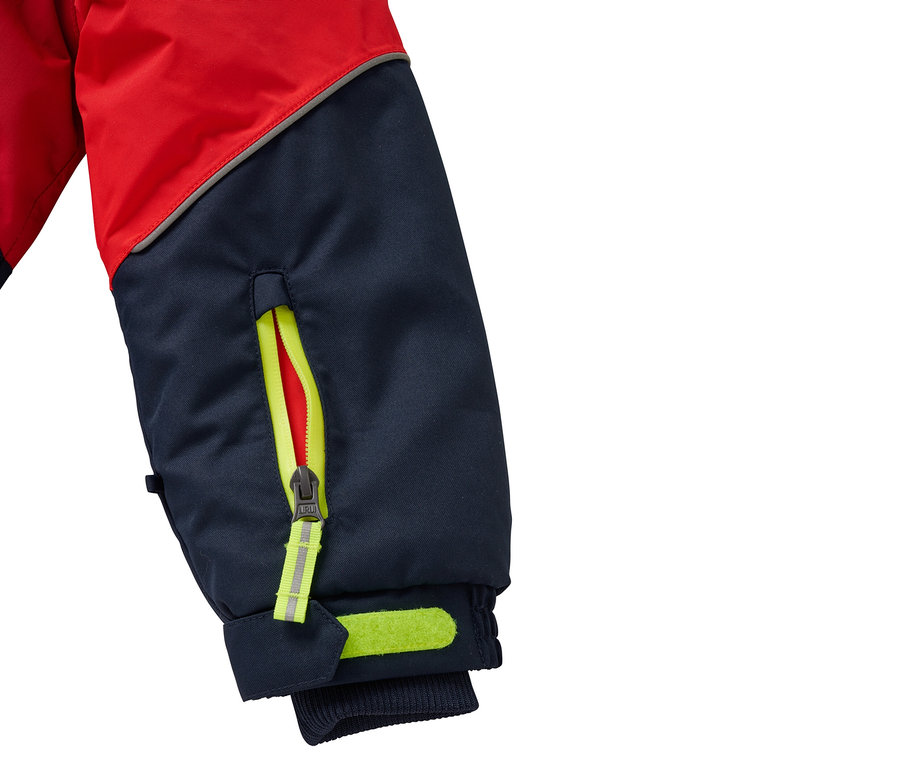 Detail eines rot-blauen Jackenärmels mit gelbem Taschenreißverschluss und reflektierenden Elementen.