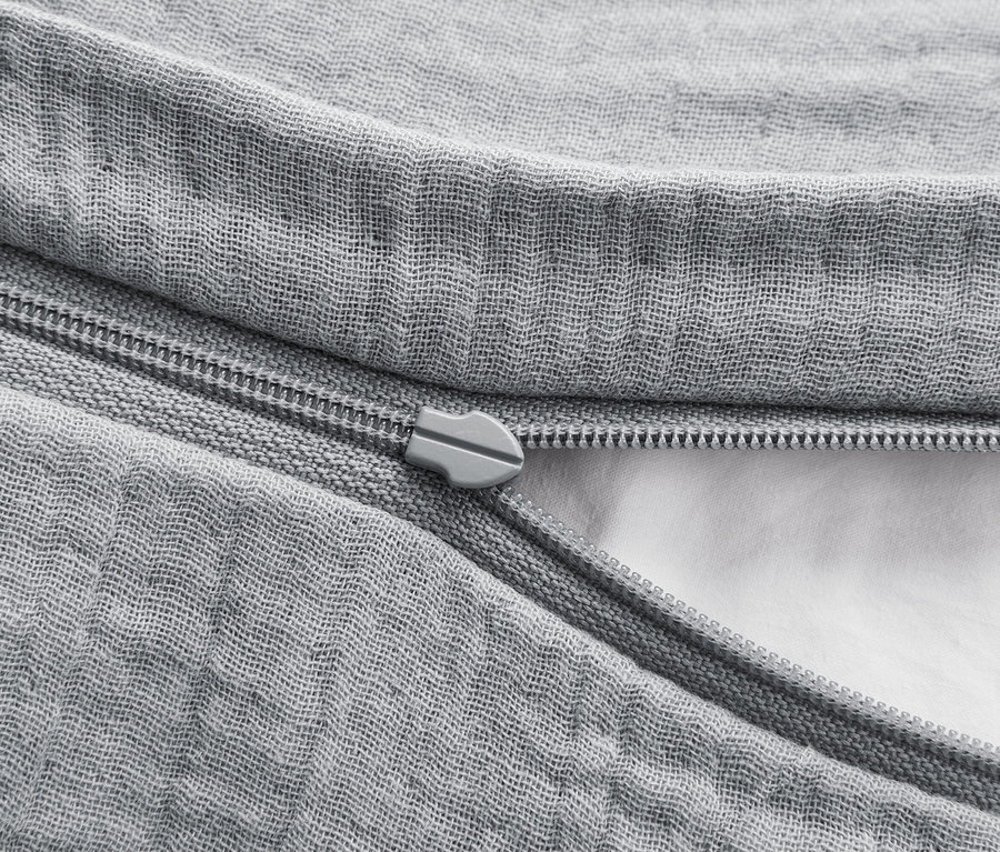 Detailaufnahme eines grauen Bettbezugs mit Reißverschluss, der teilweise geöffnet ist und eine weiße Füllung freilegt.