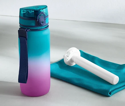 Eine Trinkflasche mit Kühlakku steht neben einem Handtuch und einer Kettlebell.