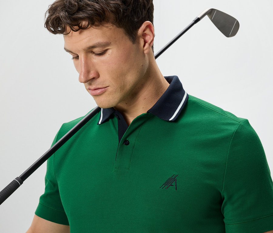Mann mit Golfschläger über der Schulter trägt ein grünes Funktions-Poloshirt.