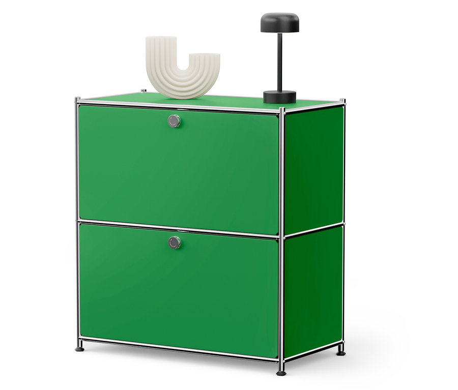 Ein grüner Schrank mit zwei Schubladen, auf dem eine weiße Dekoration und eine schwarze Lampe stehen.