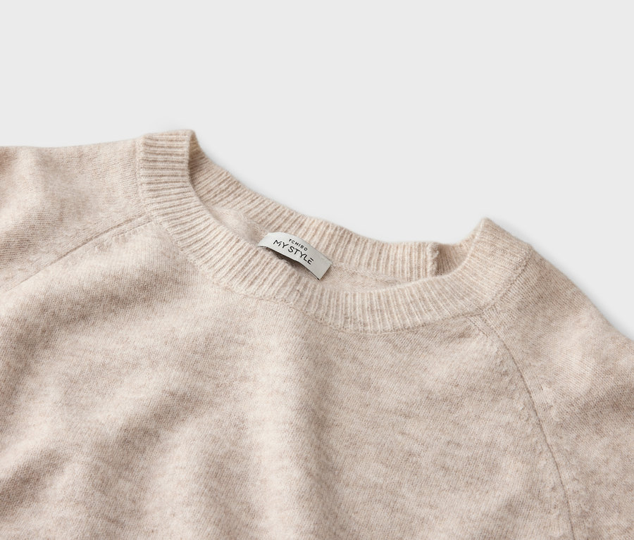 Nahaufnahme eines beigen Pullovers mit Rundhalsausschnitt und einem Etikett mit der Aufschrift "TCHIBO MY STYLE".