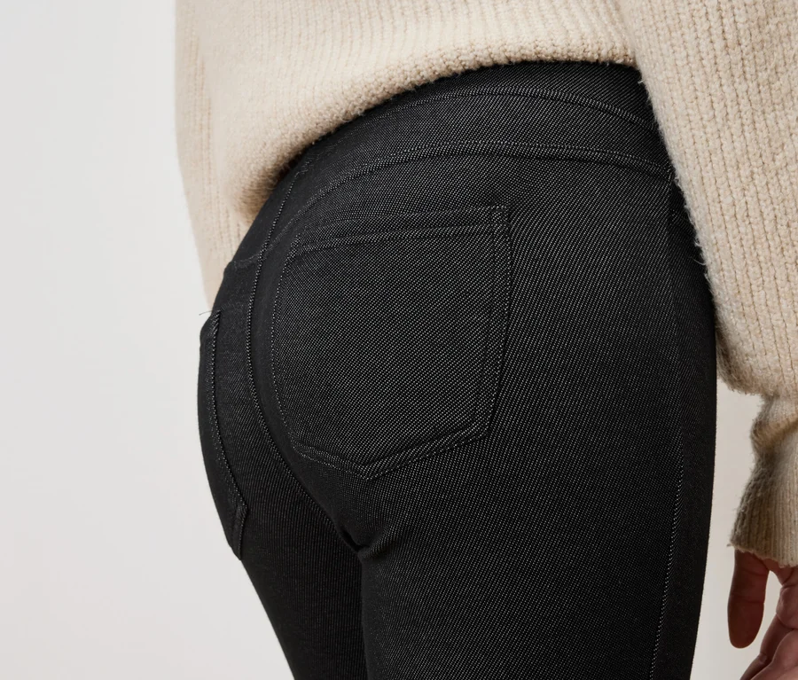 Nahaufnahme der Rückseite einer Person, die schwarze Jeans und einen beigen Pullover trägt.