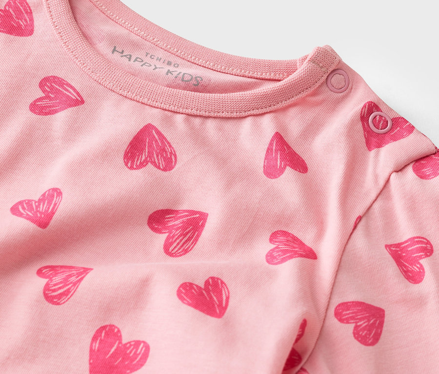 Nahaufnahme eines rosa Langarmshirts mit Herzmuster und Druckknöpfen am Kragen.