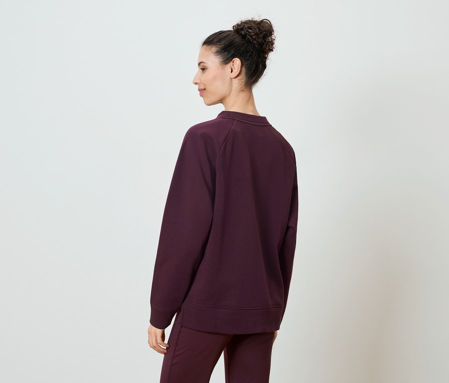 Frau von hinten in einem weinroten Pullover und passender Hose.