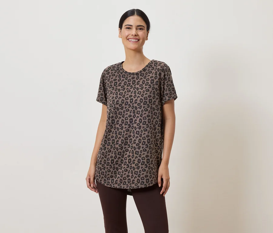 Eine Frau mit hochgesteckten Haaren trägt ein braunes Leopardenmuster-T-Shirt und braune Leggings vor einem hellen Hintergrund.