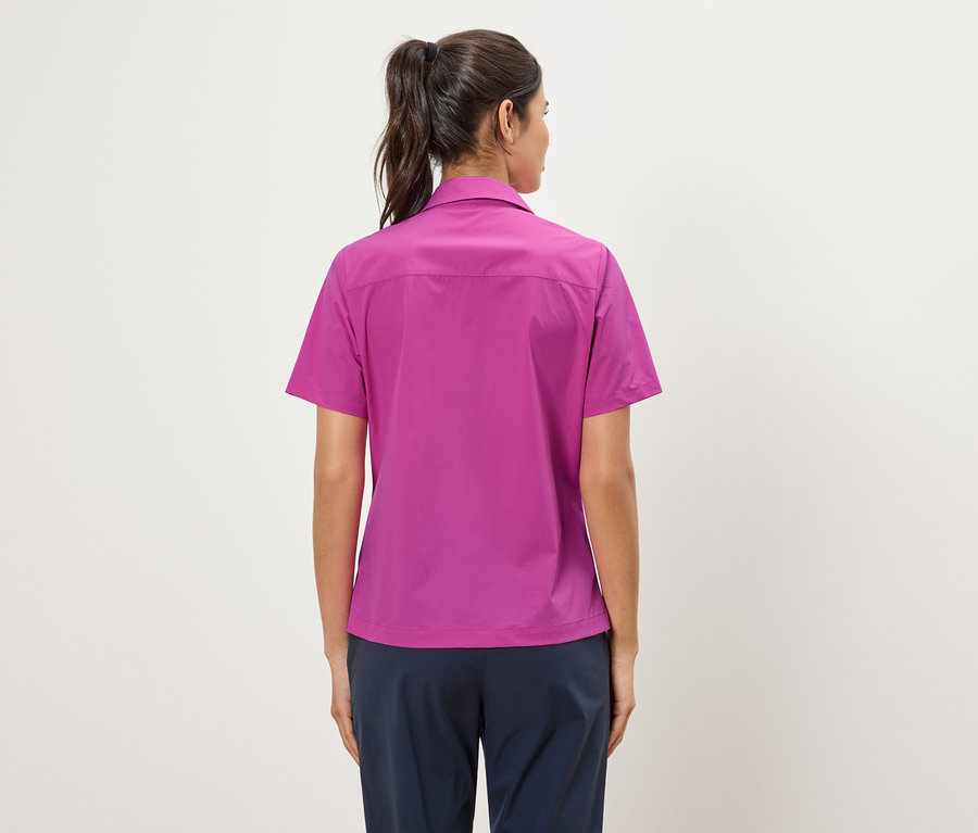 Rückansicht einer Frau mit Pferdeschwanz, die ein pinkes Hemd und marineblaue Hosen trägt.