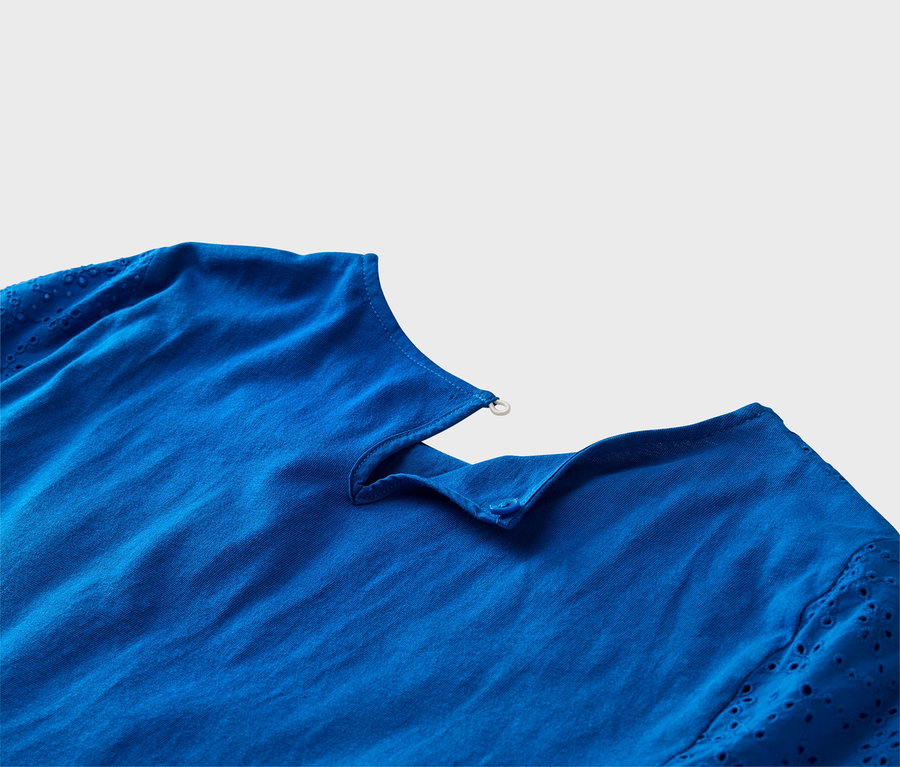 Nahaufnahme eines kobaltblauen Oberteils mit Lochstickereiärmeln und Knopfdetail.