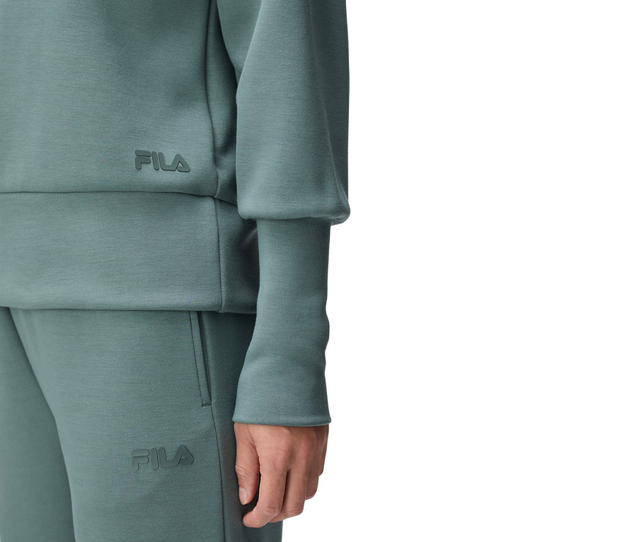 Nahaufnahme einer Person, die einen türkisfarbenen Fila-Trainingsanzug trägt, wobei das Fila-Logo auf dem Oberteil und der Hose zu sehen ist.