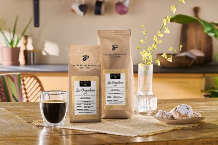 Zwei Packungen Manantiales del Frontino Colombia Kaffeebohnen neben einer Tasse Kaffee und einem Teller Kekse.