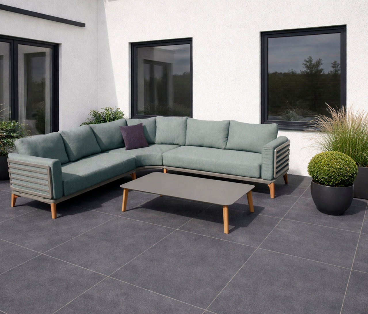 Salbeigrüne Leco Lounge-Ecke inkl. Tisch »Moss« auf einer Terrasse vor einem weißen Gebäude mit Fenstern und Pflanzen.