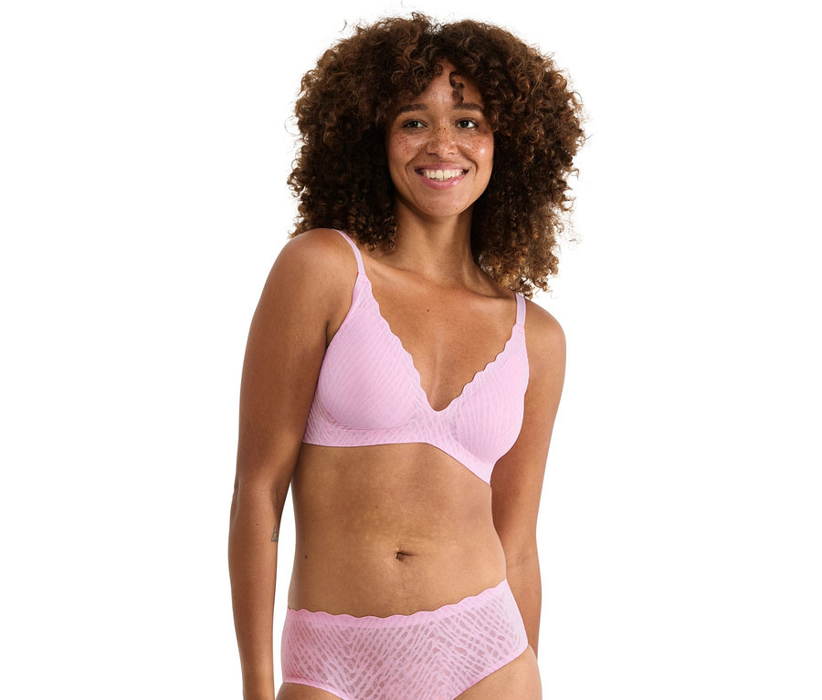Frau mit lockigem Haar trägt einen hellrosa BH und passende Unterhose.