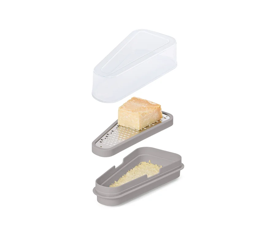 Ein graues Käsereibe-Set mit einem Stück Käse auf der Reibe, geriebenem Käse im Behälter und einem transparenten Deckel darüber.