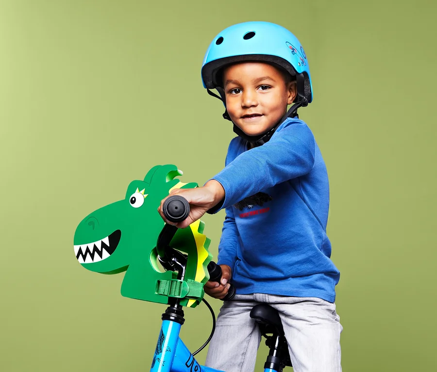 Junge mit blauem Helm auf einem Fahrrad mit Kinder-Lenkeraufsatz »Drache«.